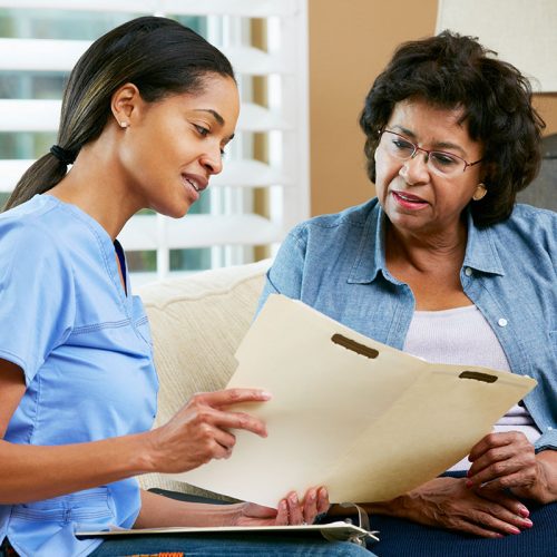 Nurse Discussing Records With Senior Female Patient During Home Nurse Discussing Records With Senior Female Patient During Home Visit Sitting On Sofa